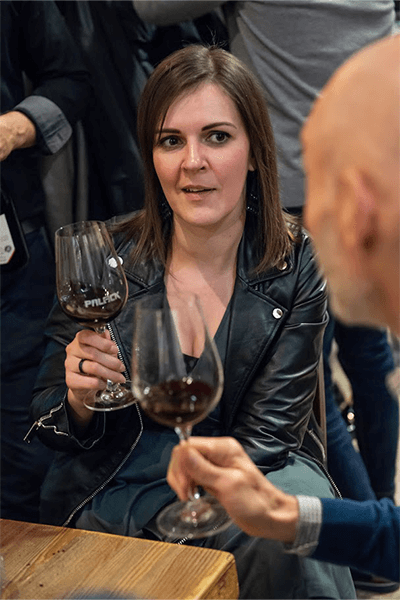 Woman in a leather jacket enjoying a glass of wine, engaged in conversation at a social gathering.