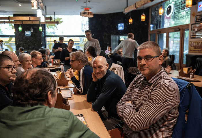 Group of people gathered around a long table in a bustling restaurant, chatting and enjoying each other's company.