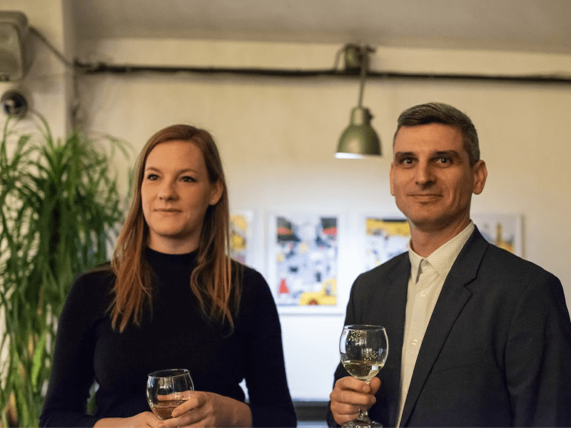 A man and woman dressed elegantly, holding glasses of wine at a social event.