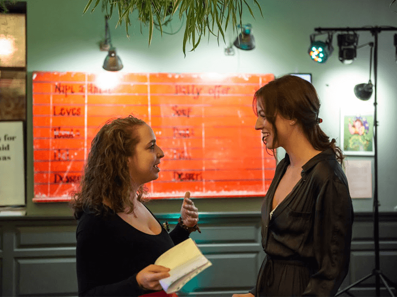 Two women engaged in a friendly conversation in a colorful, well-lit room with vibrant decorations.