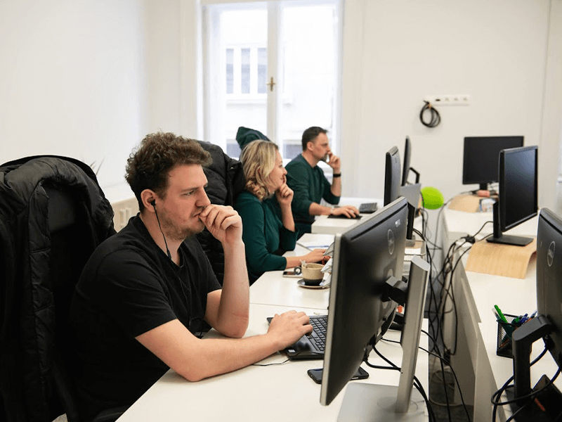 Focused individuals working at computer desks in a bright office.