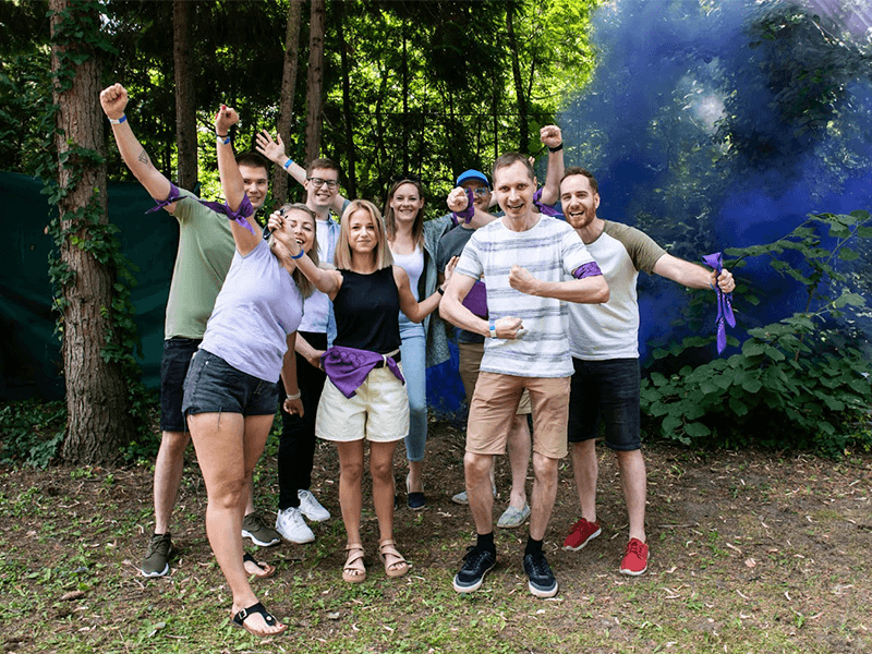 Cheerful group of people celebrating with purple smoke outdoors.